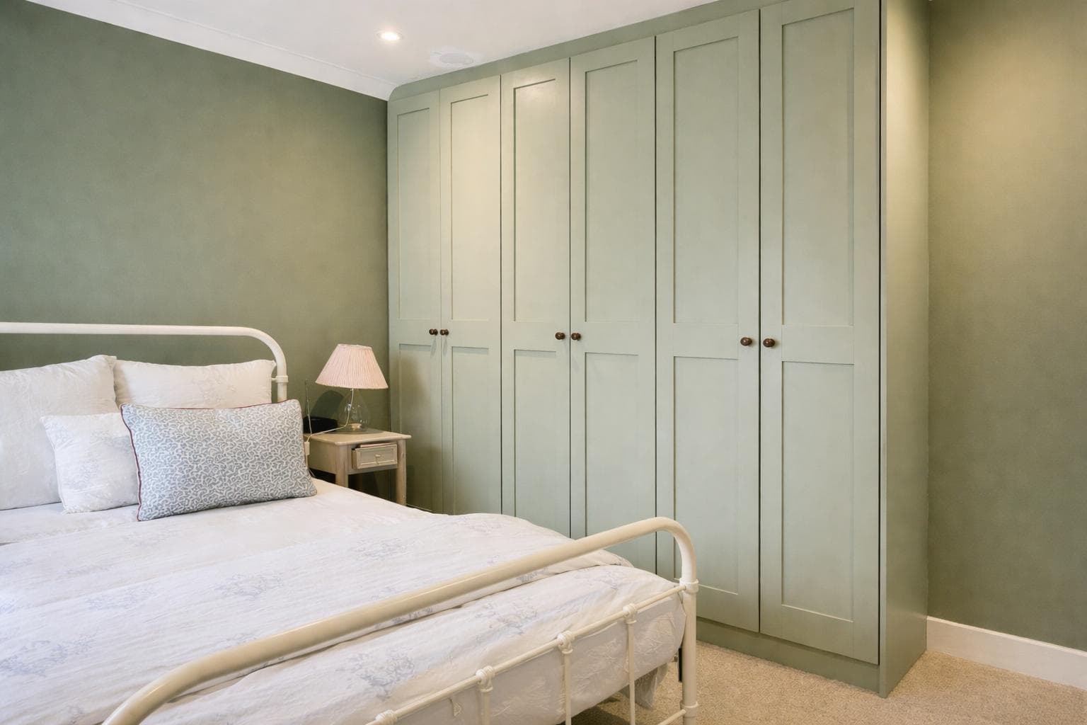 Sage green fitted wardrobes with panelled doors in a bedroom